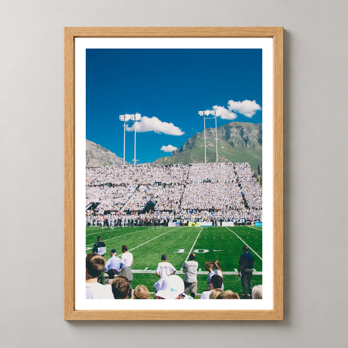Vibrant Football Stadium with Mountain Backdrop - High-Quality Print — realistic natural wood frame studio view with white border